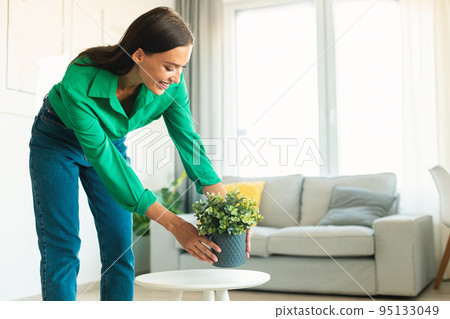 Woman Putting Plant In Pot On Table Decorating House Indoor 95133049