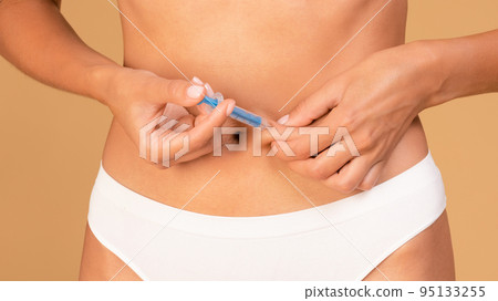 Unrecognizable woman in underwear doing injection in abdomen, holding medicine pen, closeup, panorama 95133255