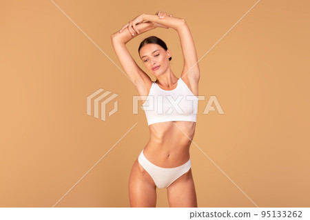 Positive young lady with perfect figure raising hands up showing armpits, isolated on beige background, free space 95133262
