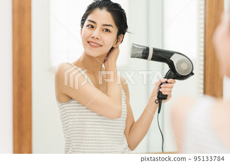 一個女人洗完澡後用吹風機吹乾頭髮 95133784
