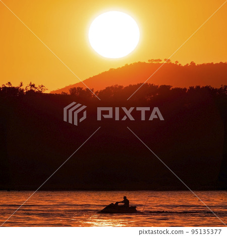 A jet ski on the sea with an orange sunset in the background  95135377