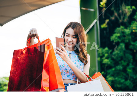 Young adult asian woman using mobile phone with shopping bags. 95136801