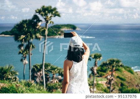 Rear view of adult asian woman relax in nature using smartphone take a selfie 95137076