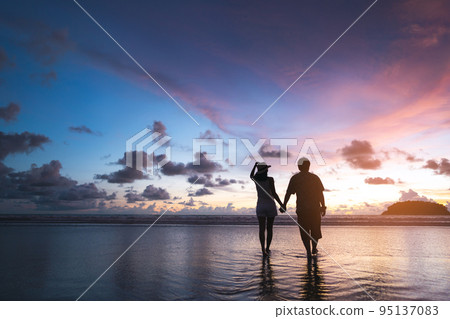 Rear view of adult tourist asian love couple holding hand on the beach with sunset sky background 95137083