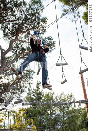 A man is resting in a rope amusement park. Vertical photo. 95137188