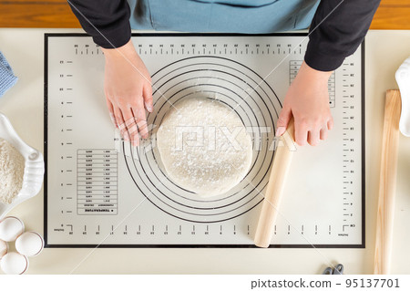 Top view of cooked wheat dough and hands of chef with rolling pin in hand on kitchen work surface 95137701