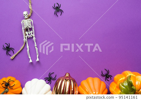 Halloween layout of garland of skeleton on a rope, glowing Jack o Lantern, pumpkins, spiders on a purple background. Flat lay horror and a terrible holiday 95141161
