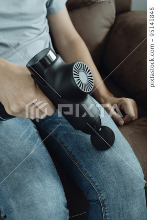 man using a massage gun on his leg 95141848
