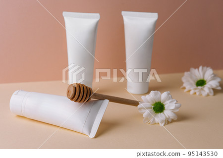 Honey infused cream with daisies. white bottles cosmetics. 95143530