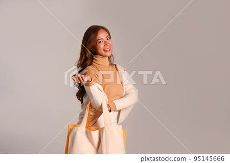 Elegant woman in warm sweater carrying tote bags standing over grey background Elegant woman in warm sweater carrying tote bags standing over grey background 95145666