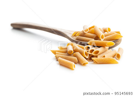 Uncooked whole grain pasta isolated on white background. Raw penne pasta on spoon. 95145693