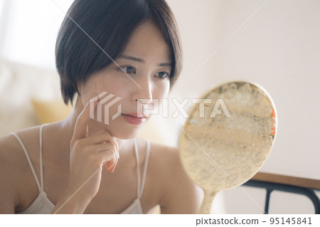 A woman with a hand mirror suffering from rough skin 95145841