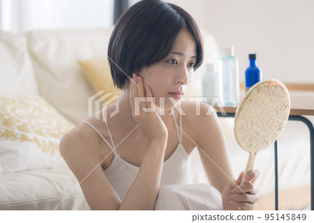 A woman with a hand mirror suffering from rough skin 95145849