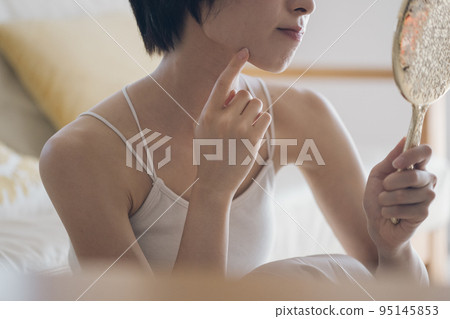 A woman with a hand mirror suffering from rough skin 95145853