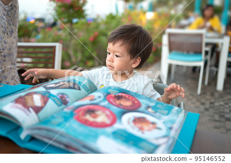 One year old baby boy looking at the menu to choose his meal in the restaurant 95146552