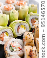 Large sushi set of various sushi rolls is served on black square metal slate. 95146570