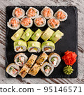 Large sushi set of various sushi rolls is served on black square metal slate. 95146571
