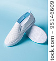 Promotional photo of pair of white women's moccasins on light blue background. 95146609