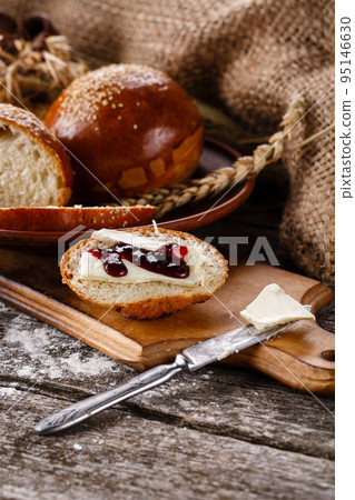 Sliced piece of freshly baked buns with butter and jam on wooden kitchen board. 95146630