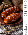 Two delicious freshly baked sweet homemade buns with crust lie on clay plate on rustic table. 95146640