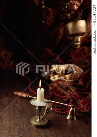 Burning candle in an old brass candlestick and carnival masks. 95147224