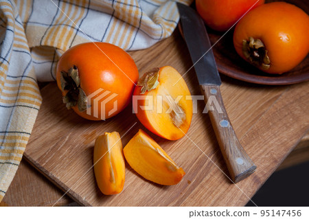 Whole ripe persimmon and sliced fruit on a wooden background.. Whole ripe persimmon and sliced fruit on a wooden background.. 95147456