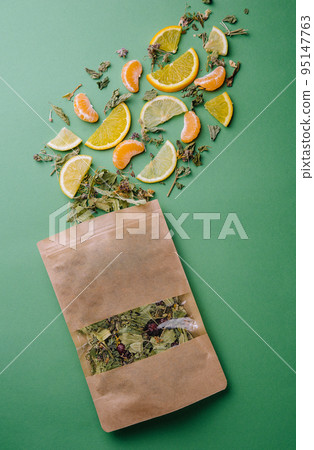 Leaf tea spilled out of a paper packet with orange and tangerine slices on green background Leaf tea spilled out of a paper packet with orange and tangerine slices on green background 95147763