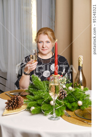 Joyful middle age woman celebrating christmas sitting behind the festive table 95148321