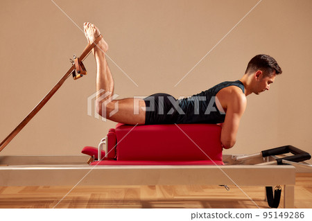 Fit man doing a lunge stretch yoga pilates exercise to strengthen and tone his muscles using a reformer in a gym 95149286
