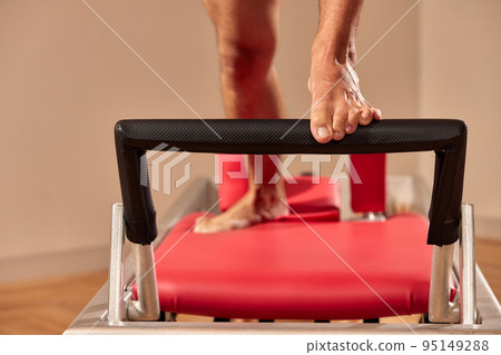 Fit man doing a lunge stretch yoga pilates exercise to strengthen and tone his muscles using a reformer in a gym 95149288