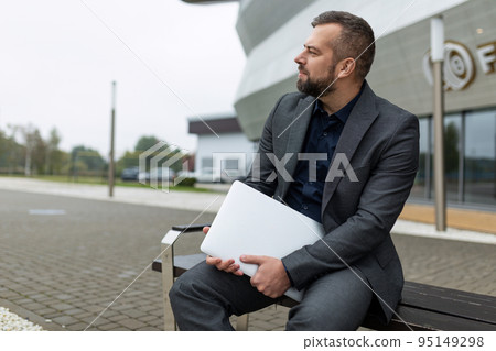 portrait of successful mature businessman with laptop sitting next to office building portrait of successful mature businessman with laptop sitting next to office building 95149298