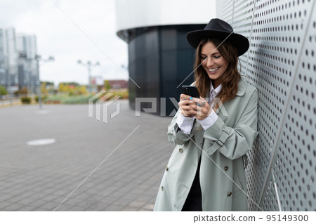 young stylish girl in a gray autumn coat and a black hat with a mobile phone in her hands with a 95149300