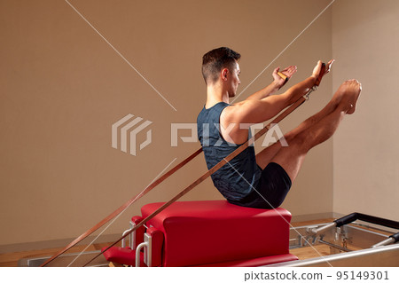 Fit man doing a lunge stretch yoga pilates exercise to strengthen and tone his muscles using a reformer in a gym 95149301