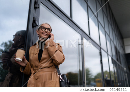 Senior woman head in stylish business clothes speaks on a mobile phone against the backdrop of an Senior woman head in stylish business clothes speaks on a mobile phone against the backdrop of an 95149311