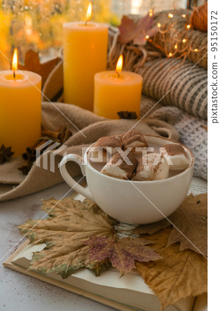 Celebrating autumn holidays at cozy home with cup hot chocolate marshmallows cacao on the windowsill Hygge atmosphere Thanksgiving candle on cozy knitted sweater in warm yellow lights Celebrating autumn holidays at cozy home with cup hot chocolate marshmallows cacao on the windowsill Hygge atmosphere Thanksgiving candle on cozy knitted sweater in warm yellow lights 95150172