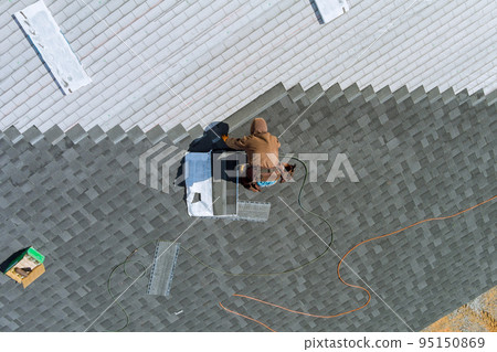 Worker uses an air hammer to nail new shingles bitumen for roof using top view from above 95150869
