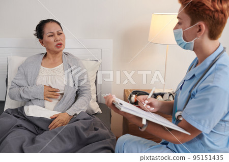 Asian sick patient talking about her problems to nurse while she asking question and filling the card at home Asian sick patient talking about her problems to nurse while she asking question and filling the card at home 95151435