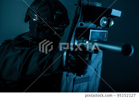 Police special forces fighter, assault team member, tactical group officer in black uniforms, aiming with silenced pistol while hiding behind, covering himself with ballistic shield, toned colorized 95152127
