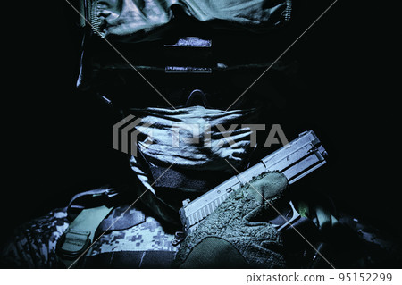 Special operations forces soldier in combat helmet with hidden behind balaclava and dark glasses face posing with sidearm service pistol in hand. Tone, high contrast, cropped on black background 95152299
