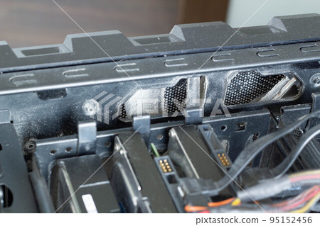 Very dirty computer fan blades for cooling against the background of hard drives, HDD and SSD drives, DVD and CD drives and other devices in a computer tower. Electronic equipment. Electronics repair 95152456