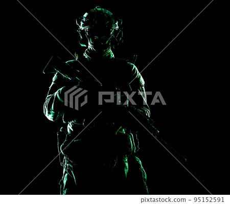 Army special forces elite soldier with hidden behind mask and glasses face, battle helmet, tactical radio headset, standing with assault rifle equipped silencer in darkness, contour shot 95152591