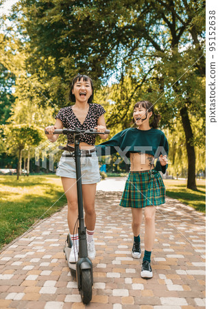 Cute slim young girls riding a scooter in the park Cute slim young girls riding a scooter in the park 95152638