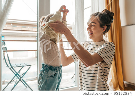 Loving mother dressing her daughter by the window 95152884