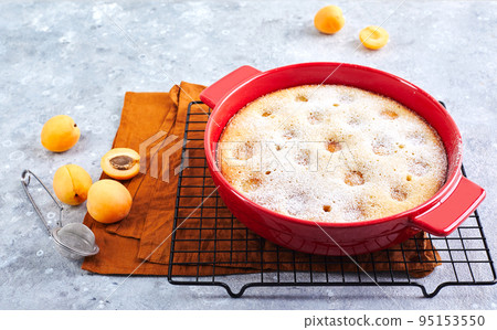 Delicious homemade apricot pie with fresh apricots in red baking dish on gray background. Summer fruit pie. 95153550