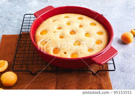 Delicious homemade apricot pie with fresh apricots in red baking dish on gray background. Summer fruit pie. 95153551