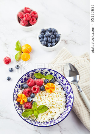 Cottage cheese in bowl garnished with raspberries, blueberries, physalis and mint leaves on white background Cottage cheese in bowl garnished with raspberries, blueberries, physalis and mint leaves on white background 95153655