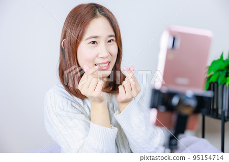 Woman making finger heart in front of mobile phone 95154714