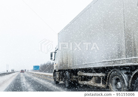 White blank modern delivery big shipment cargo commercial semi trailer truck moving fast on motorway road at heavy snowfall in winter. Business distribution logistics service. Lorry driving highway 95155006