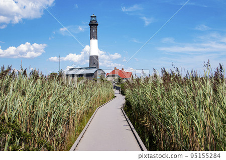 Looking down the boardwalk at the Fire Island Lighthouse surrounded by tall beach grass Looking down the boardwalk at the Fire Island Lighthouse surrounded by tall beach grass 95155284