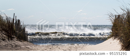 Panaromic view looking through the sand dunes of large ocean waves crashing on the beach Panaromic view looking through the sand dunes of large ocean waves crashing on the beach 95155291